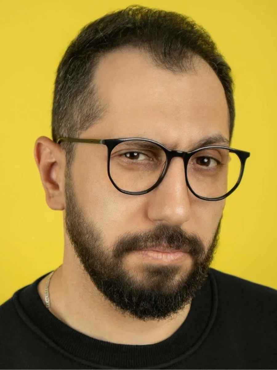 Mohamed Galal, portrait with glasses on a yellow background.
